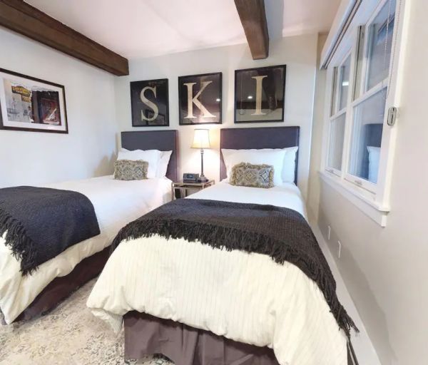 This image shows a cozy bedroom with two single beds, a bedside table with a lamp, and wall art spelling 