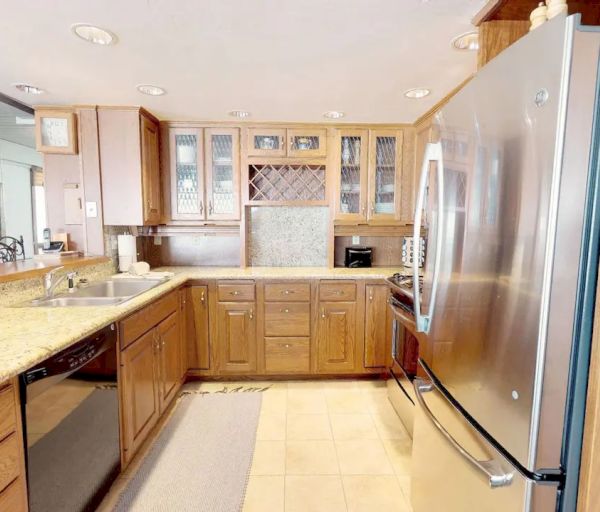 A modern kitchen featuring wooden cabinets, a double sink, a dishwasher, a large refrigerator, and granite countertops with a breakfast bar.
