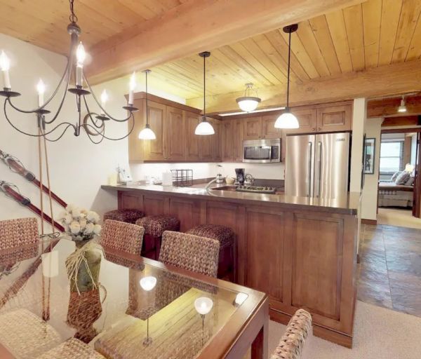 A cozy kitchen and dining area with wooden accents, a chandelier, retro skis for decoration, stainless steel appliances, and woven seating.