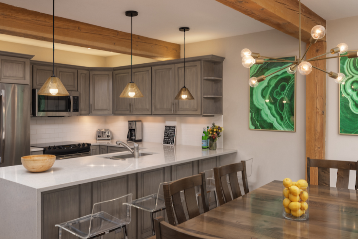 The image features a modern kitchen with wood accents, sleek appliances, a dining table, and decorative wall art.