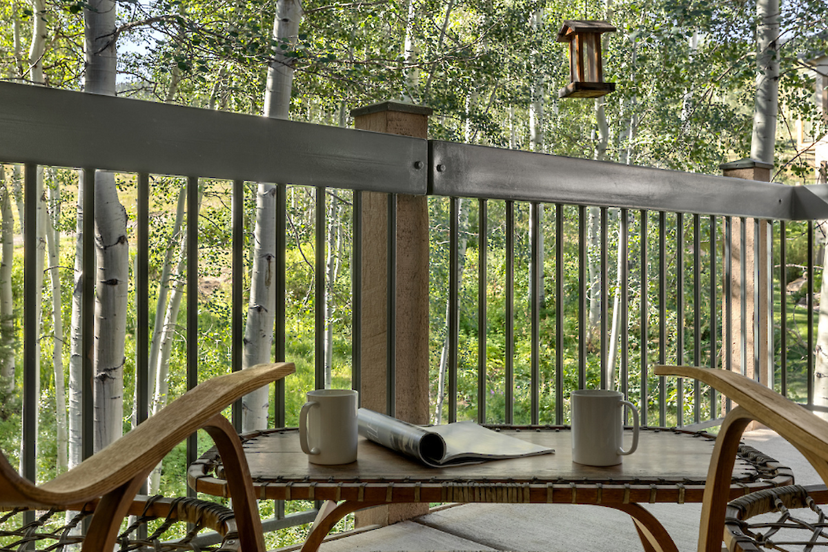 A cozy balcony scene with two chairs, a small table, coffee cups, and views of green trees in the background. Perfect for relaxation.
