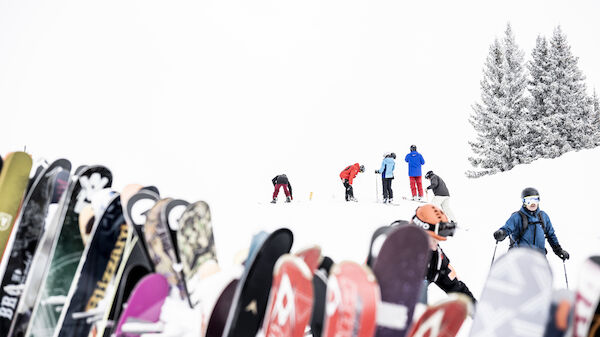 A group of skiers on a snowy slope with trees in the background, and a row of skis standing upright in the foreground.